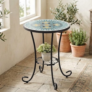 May include: A round side table with a black metal frame and a mosaic tile top featuring a teal, yellow, and white geometric pattern. The table includes a lower circular metal shelf holding a small white pot with green and white flowers.