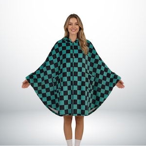 Pode incluir: Um poncho com capuz em um padrão xadrez preto e verde-azulado. O poncho tem um fecho de botão no pescoço e dois bolsos frontais. A peça de roupa é feita de um material macio e felpudo.