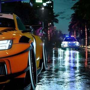 Könnte beinhalten: Ein orangefarbener Sportwagen mit schwarzen Akzenten steht nachts auf einer nassen Straße. Im Hintergrund ein Polizeiauto mit blinkenden blauen und roten Lichtern. Palmen und Stadtlichter spiegeln sich in der nassen Fahrbahn.