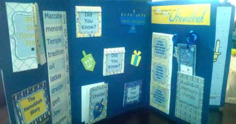 K&ouml;nnte beinhalten: Ein blaues und gelbes Hanukkah-Bulletin Board mit den Worten "The Hanukkah Story" und "Dreidel" darauf. Es gibt auch mehrere "Did You Know?"-Karten mit Fakten &uuml;ber Hanukkah.