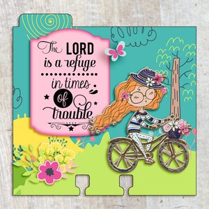 Puede incluir: Una tarjeta rosa y blanca con una cita sobre el Se&ntilde;or siendo un refugio en tiempos de problemas. La tarjeta presenta a una ni&ntilde;a de dibujos animados montando una bicicleta con flores en una cesta.