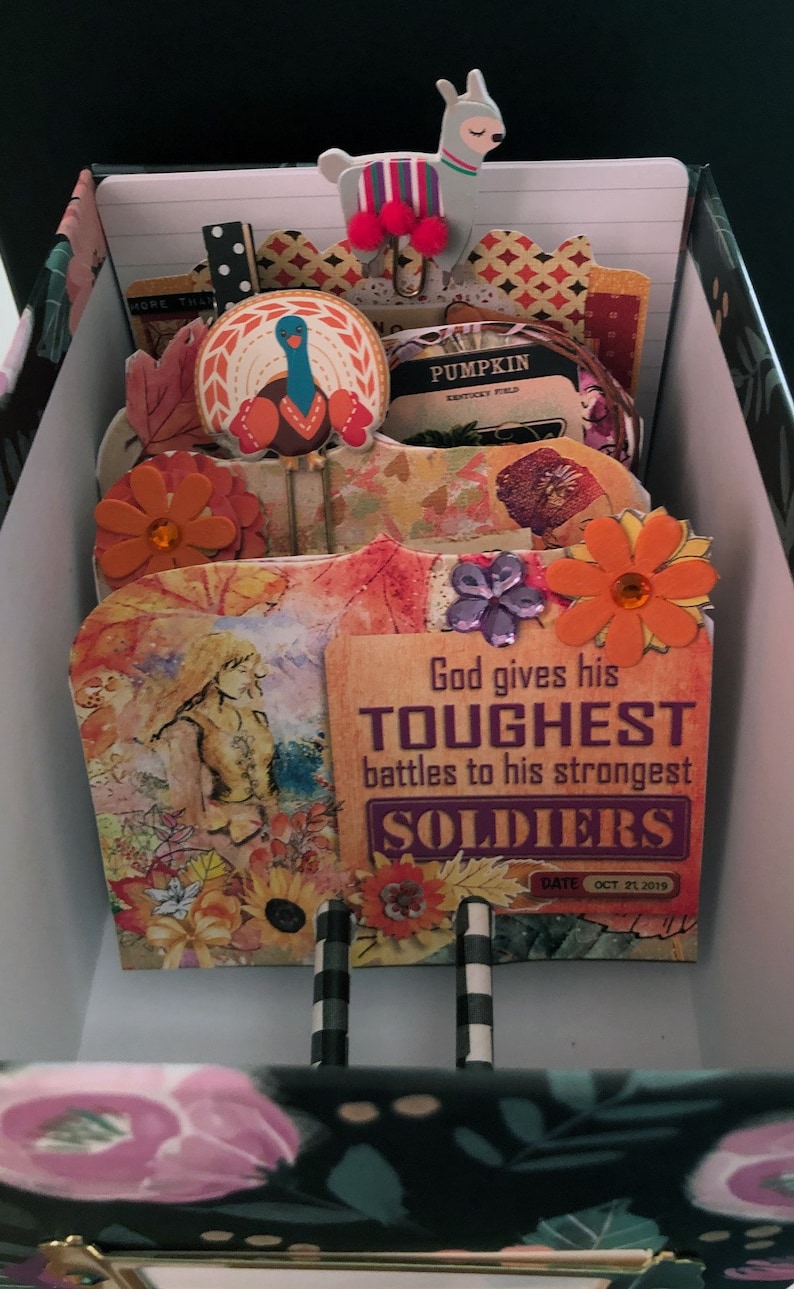 May include: A scrapbook page with an autumn theme. The page features a quote about God giving his toughest battles to his strongest soldiers. The page is decorated with autumn-themed embellishments, including a turkey, flowers, and leaves.