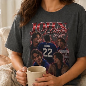Pode incluir: Uma t-shirt de manga curta em cinzento escuro mesclado com uma impress&atilde;o gr&aacute;fica de estilo vintage com o texto JOHN LOGAN Off Campus. O design inclui v&aacute;rios retratos fotogr&aacute;ficos de um homem e a parte de tr&aacute;s de uma camisola com o nome LOGAN e o n&uacute;mero 22.