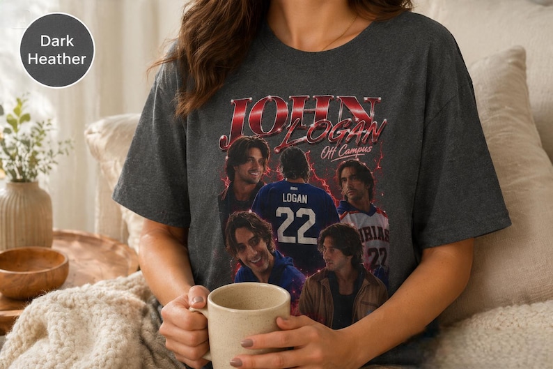 Pode incluir: Uma t-shirt de manga curta em cinzento escuro mesclado com uma impress&atilde;o gr&aacute;fica de estilo vintage com o texto JOHN LOGAN Off Campus. O design inclui v&aacute;rios retratos fotogr&aacute;ficos de um homem e a parte de tr&aacute;s de uma camisola com o nome LOGAN e o n&uacute;mero 22.