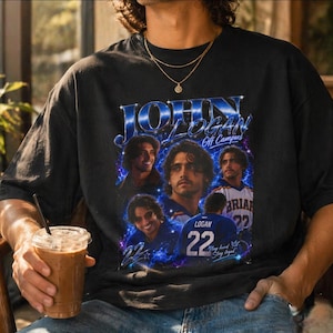Puede incluir: Una camiseta negra de manga corta con un estampado gráfico de John Logan. El diseño incluye varios retratos, el texto "JOHN LOGAN" en azul, "Off Campus", "BRIAR 22" y "Stay loyal" junto con efectos de rayos de color azul.