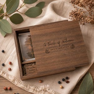 May include: A rectangular dark brown wooden box with a sliding lid featuring the engraved text A Touch of Autumn PHOTOGRAPHY and two leaf icons. Inside, a small photograph and a wooden block engraved with Mr and Mrs Saunders 2nd June 2024.