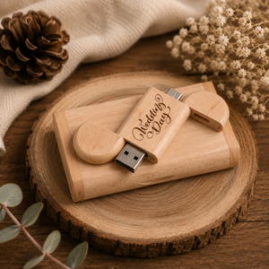 Op de afbeelding: Een lichtgekleurde houten USB-stick met een bijpassend rechthoekig houten doosje. De USB-stick is voorzien van de gegraveerde tekst Wedding Day in een cursief lettertype en bevat een losse houten dop voor de metalen connector.