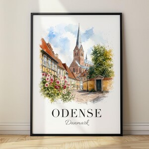 May include: A framed wall art print featuring a watercolour illustration of a street scene in Odense, Denmark. The image depicts a tall church spire, half-timbered houses, pink flowers, and a cobblestone path. The text reads ODENSE Danmark.