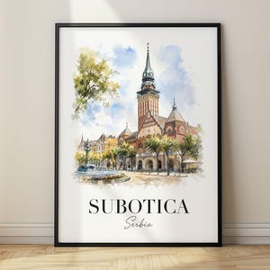 Pode incluir: Uma impressão de arte em aguarela emoldurada que retrata a Câmara Municipal de Subotica na Sérvia, com uma torre de relógio alta, uma fonte em primeiro plano e árvores verdes sob um céu azul. O texto SUBOTICA e Serbia está impresso a preto.