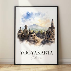 Peut inclure: Une affiche encadrée représentant une illustration à l'aquarelle du temple de Borobudur en Indonésie avec une statue de Bouddha assise, des stupas en pierre et un paysage montagneux. Le texte YOGYAKARTA Indonesia est imprimé en noir en bas.