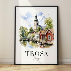 Puede incluir: Una lámina enmarcada con una ilustración en acuarela de una escena urbana sueca con el campanario de una iglesia, casas de madera roja, un canal y un pequeño bote. El texto TROSA y Sverige está impreso en negro en la parte inferior.