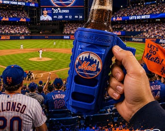 Puede incluir: Un enfriador de bebidas de plástico azul con asa, que presenta el texto Assault Koozie y un logotipo de los New York Mets. El enfriador sostiene una botella de vidrio con líquido marrón, frente a un estadio de béisbol por la noche.