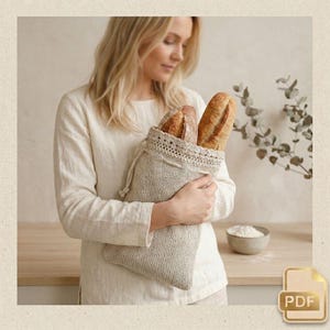 Può includere: Una borsa in maglia beige con coulisse contenente due pagnotte croccanti. La borsa presenta un bordo superiore testurizzato in stile intrecciato con un cordino abbinato. Il tessuto ha un motivo a maglia visibile e coerente su tutto il corpo.
