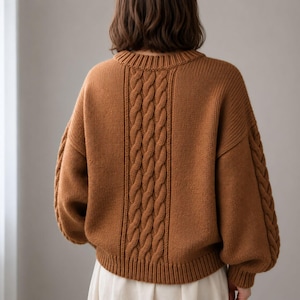 May include: A long-sleeved, crew-neck sweater in a solid warm brown color. The garment features a prominent vertical cable-knit pattern running down the center of the back and along the outer length of each sleeve, with ribbed cuffs and hem.