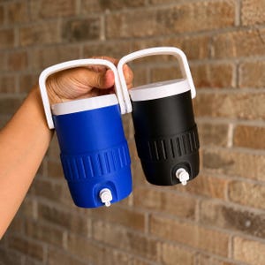 May include: Two insulated water coolers, one blue and one black, each with a white handle and lid. The coolers have a spigot for dispensing liquids. The background is a brick wall.