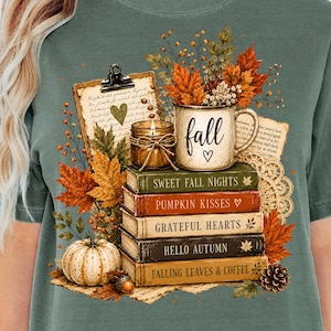 Pode incluir: Uma t-shirt verde sálvia com um gráfico de uma pilha de livros intitulados Sweet Fall Nights, Pumpkin Kisses, Grateful Hearts, Hello Autumn e Falling Leaves & Coffee, encimada por uma caneca com a etiqueta Fall, folhas de outono e uma abóbora.