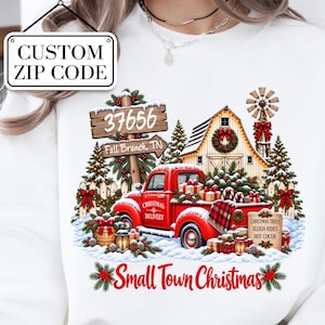 May include: A white sweatshirt featuring a graphic of a red truck with the text Christmas Delivery, a wooden sign reading 37656 Fall Branch, TN, a barn, a windmill, pine trees, gifts, and the text Small Town Christmas, Christmas Trees, Sleigh Rides, Hot Cocoa.