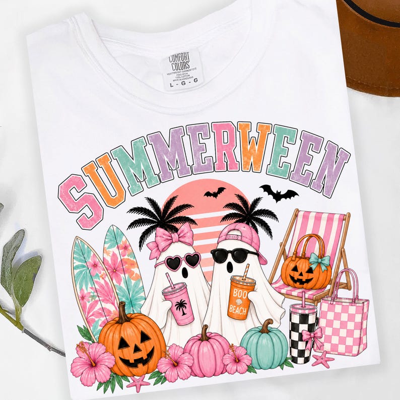 May include: A white t-shirt featuring a graphic with the text SUMMERWEEN in pastel colors. The design includes two ghosts, one wearing a pink bow and heart sunglasses, the other a pink cap and black sunglasses, with surfboards, pumpkins, and beach gear.