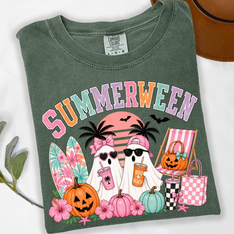 May include: A dark olive green t-shirt featuring the text SUMMERWEEN in pastel letters. The graphic includes two ghosts, one with a pink bow and heart sunglasses, the other with a pink cap and black sunglasses, surfboards, pumpkins, and a beach chair.