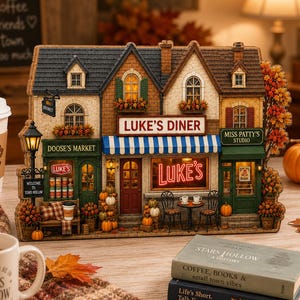 Pode incluir: Um modelo em miniatura detalhado de uma rua com o Luke's Diner, Doose's Market e Miss Patty's Studio. A estrutura inclui janelas iluminadas, um toldo de riscas azuis e brancas, folhagem de outono e abóboras expostas no exterior.