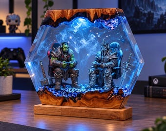 May include: A hexagonal resin lamp featuring a wooden frame and base, containing two miniature fantasy figures sitting in gaming chairs. The interior is illuminated with blue light and swirling smoke effects, with a hammer and sword placed beside the figures.