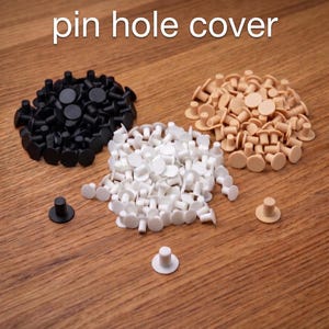 Può includere: Immagine di copri fori per perni Ikea Besta in nero, bianco e beige. I copri fori sono piccoli, rotondi e progettati per adattarsi ai fori dei perni. L'immagine è scattata su una superficie di legno.