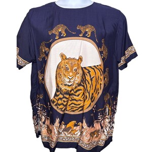 May include: Navy blue short-sleeve shirt featuring a large tiger illustration in a circular frame. The shirt has a repeating pattern of leopards and floral accents. The tiger is orange and black, with a white background.