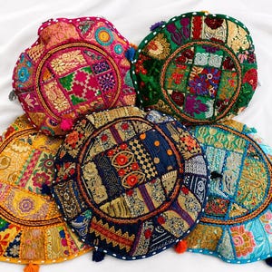 Può includere: Cinque cuscini da pavimento rotondi con complessi disegni patchwork, motivi floreali ricamati, accenti in filo metallico e piccole nappe colorate lungo i bordi. I cuscini sono realizzati nelle tonalità rosa, verde, giallo, blu e blu navy.