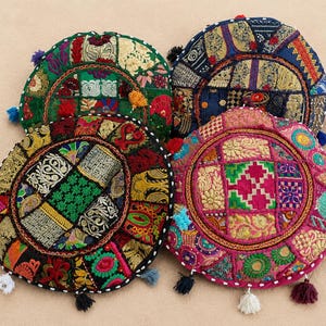 May include: Four round floor cushions featuring intricate patchwork designs with embroidered patterns in vibrant colors including green, blue, pink, and black. Each cushion is decorated with small fabric tassels along the edges.