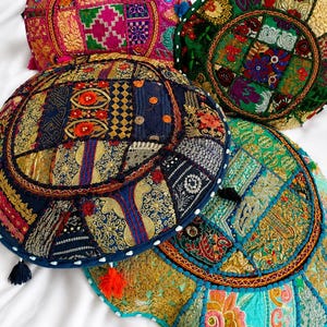 Könnte beinhalten: Vier runde Bodenkissen mit komplexen Patchwork-Mustern, lebendigen Stickereien, metallischem Goldfaden und kleinen dekorativen Quasten. Die Kissen zeigen eine Vielzahl von Farben, darunter tiefes Blau, leuchtendes Pink, Smaragdgrün und Türkis.