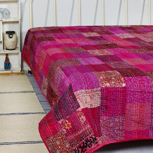 Può includere: Una trapunta patchwork composta da vari quadrati di tessuto rosa, magenta e rosso scuro con intricati motivi floreali e geometrici. La trapunta presenta dettagli di cuciture a vista su tutta la superficie.