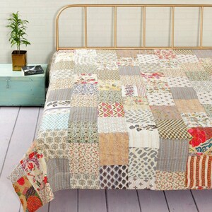 Può includere: Una trapunta patchwork composta da una varietà di pannelli quadrati in tessuto con diversi motivi floreali, geometrici e astratti in tonalità tenui di beige, rosa, blu e verde, cuciti insieme con dettagli in filo bianco visibili su tutta la superficie.