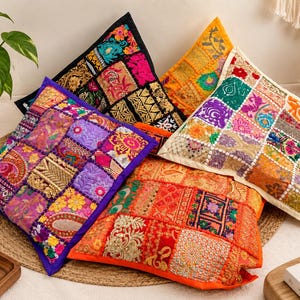 Peut inclure: Un ensemble de quatre coussins carrés présentant des motifs en patchwork complexes avec des broderies multicolores vives, des paillettes et des accents de fils métalliques. Chaque coussin affiche un agencement unique de carrés de tissu dans des tons de violet, orange, noir et crème.