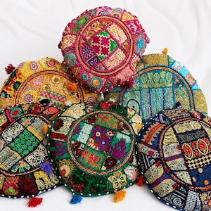 May include: A collection of six round floor cushions featuring intricate patchwork designs with vibrant embroidery, metallic thread accents, and small colourful tassels attached to the edges. Each cushion displays a unique combination of fabric patterns.