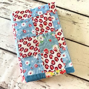 May include: A rectangular fabric cover featuring a patchwork design of alternating squares. The pattern consists of light blue squares with white and red floral prints and cream-colored squares with a repeating red paisley-like motif.