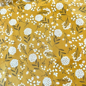 May include: Mustard yellow fabric with a repeating floral pattern. White, round flower clusters and small white flowers are interspersed with dark brown stems and leaves. Two clear glass jars are visible in the upper left corner.