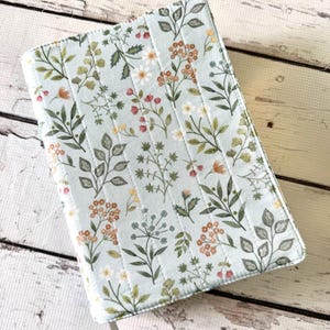 May include: A light blue quilted book cover with a floral pattern. The cover features a repeating design of green leaves, small white and red flowers, and tan flower clusters. The cover has a white ribbon bookmark.