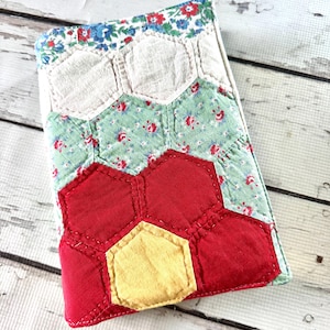 May include: A rectangular fabric cover featuring a patchwork design of stitched hexagons. The pattern includes solid red, solid yellow, and light green floral fabric pieces, topped with white hexagons and a blue and red floral border at the edge.