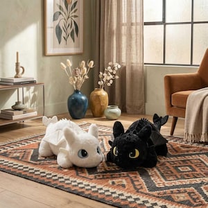May include: Two plush dragon toys, one white and one black, are displayed on a patterned rug. The white dragon has blue eyes and white wings. The black dragon has yellow eyes and black wings. The toys are in a living room setting.