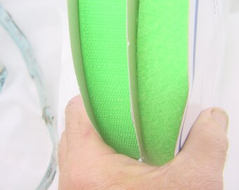 May include: Two rolls of bright green hook and loop fastener tape. The tape is folded in half and held in a hand.