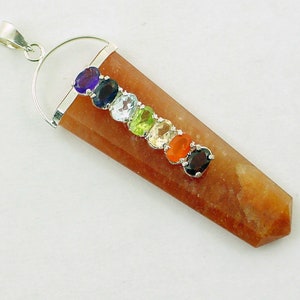 Puede incluir: Un colgante con un cristal marrón alargado y una fianza plateada. Siete piedras preciosas ovaladas de varios colores están engastadas a lo largo del cristal. Las piedras incluyen púrpura, azul, celeste, verde, amarillo, naranja y negro.