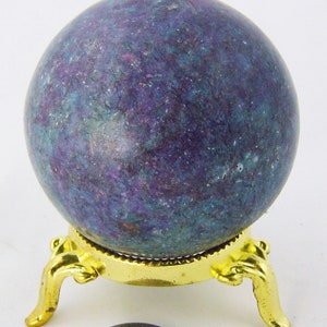 May include: A purple and green sphere on a gold metal stand with three legs. The sphere is about the size of a US quarter.