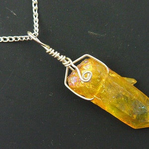 Op de afbeelding: Een gouden draadgewikkelde kristallen hangerketting. De kristal is een heldere, gefacetteerde, gele kwarts met iriserende regenboogflitsen. De hanger is bevestigd aan een zilveren ketting.