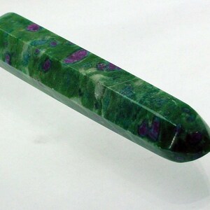May include: A green and pink gemstone wand with a faceted, pointed tip. The wand is made of a polished, translucent stone with a swirling pattern of green, pink, and white.