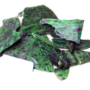 May include: A collection of rough-cut ruby in zoisite stones. The stones are a mix of green and black with purple accents. The pieces vary in size and shape, with a natural, unpolished appearance. The background is plain white.