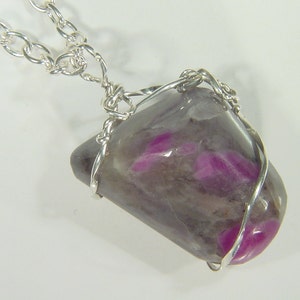 May include: A silver chain necklace with a wire-wrapped pendant featuring a grey and pink gemstone.