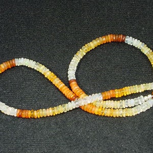 May include: A necklace made of small, round, multi-colored opal beads. The beads are arranged in a graduated pattern, with the darkest beads at the top and the lightest beads at the bottom. The necklace is strung on a silver chain.