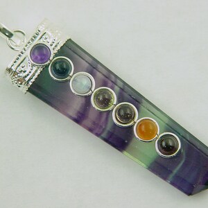 Puede incluir: Un colgante de plata con una piedra de fluorita púrpura y verde y siete piedras de chakra. Las piedras son amatista, ónix negro, piedra lunar, peridoto, cornalina, citrino y jaspe rojo.
