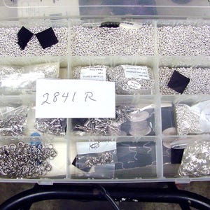 May include: A clear plastic storage box filled with various silver metal chain links and jump rings. The box is labeled "2841 R".
