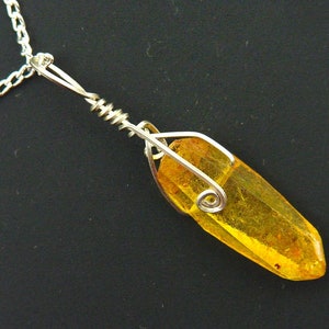 Op de afbeelding: Een zilveren ketting met een hanger van gele barnsteen, gewikkeld in zilverdraad.